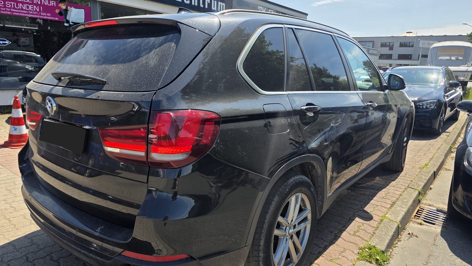 Schwarzer BMW X5 mit Dellen und Unfallschaden an der hinteren Seitenwand auf dem Werkstatthof