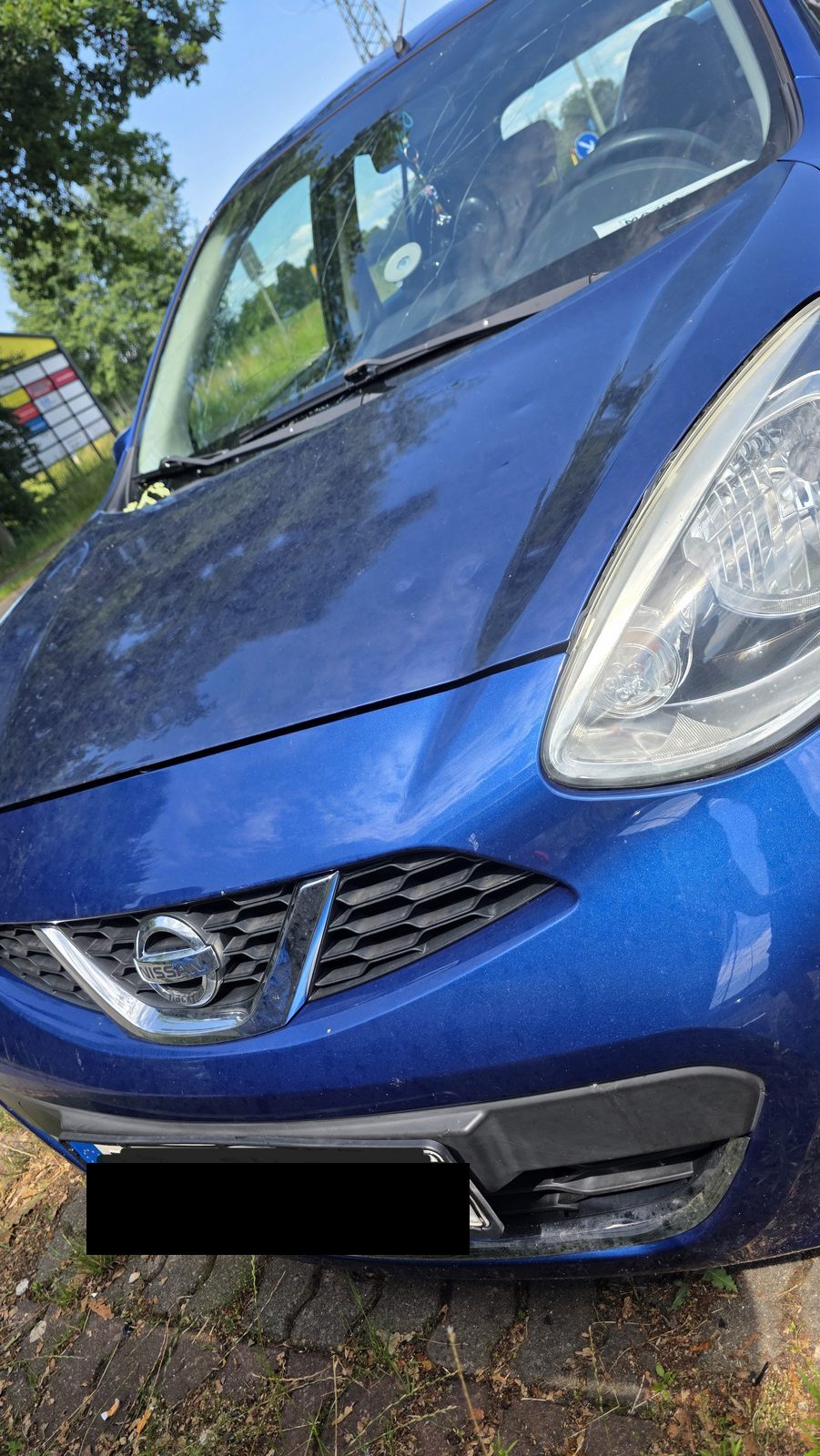 Blauer Nissan mit gesprungener Windschutzscheibe und Schäden an der Motorhaube als Kaskoschaden in Norddeutschland