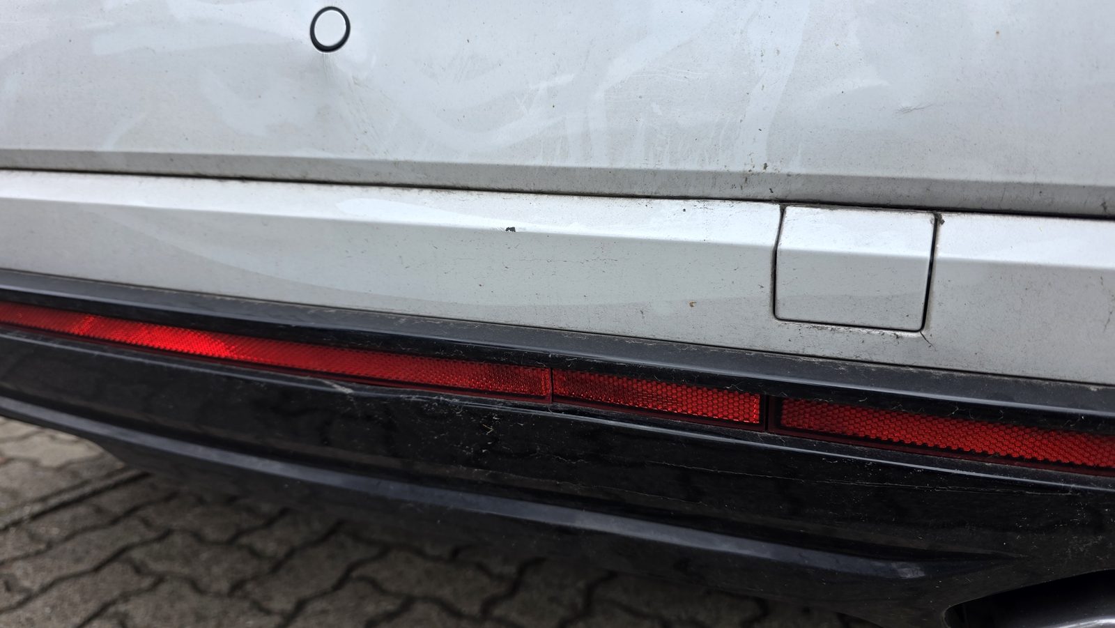 Nahaufnahme eines silbernen Fahrzeughecks mit Kratzern und Schürfspuren am Stoßfänger nach einem Parkrempler