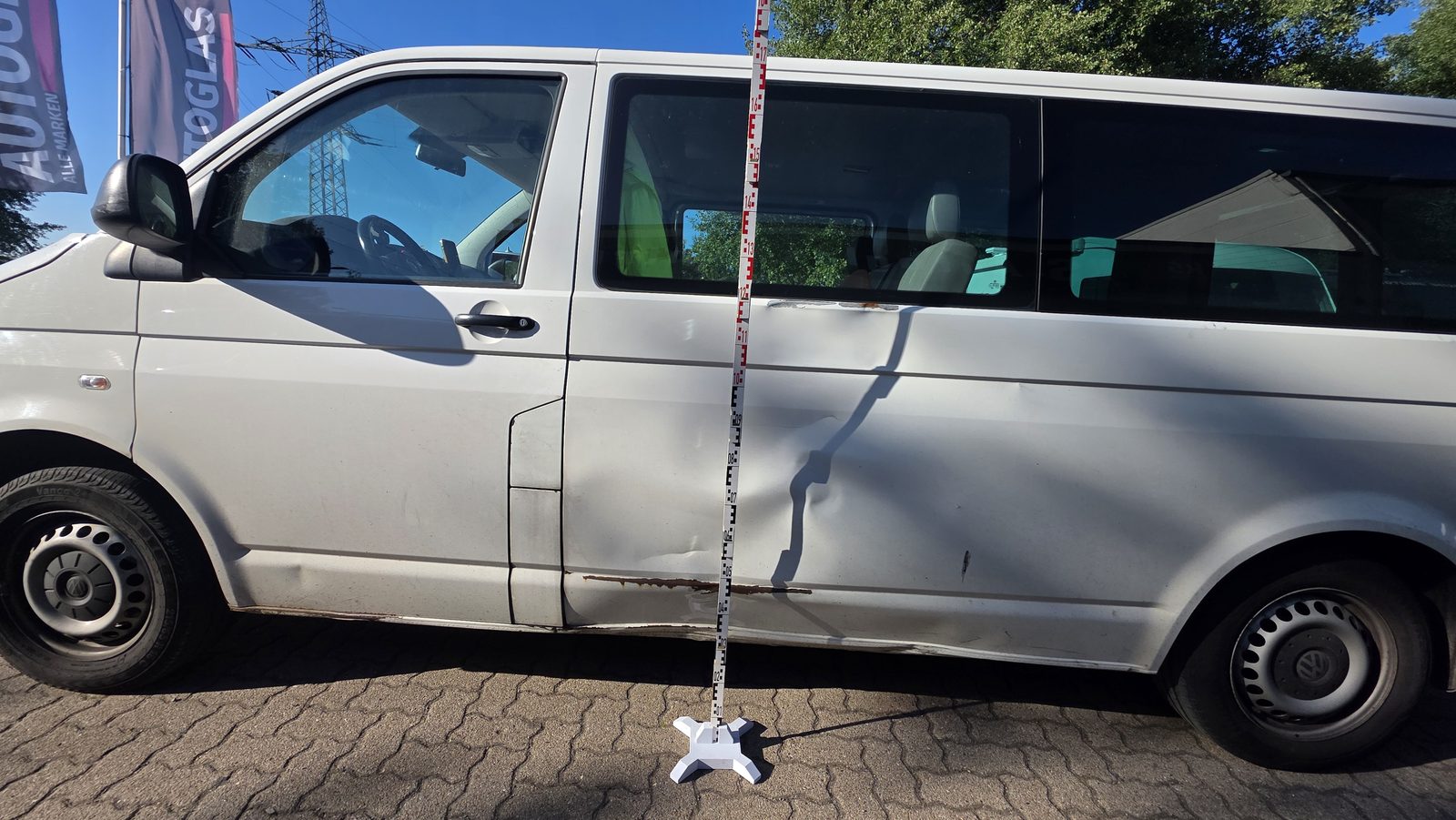 Weißer VW T5 mit deutlicher Delle an der Seitenwand wird mit Fotomessleiste für ein Gutachten dokumentiert